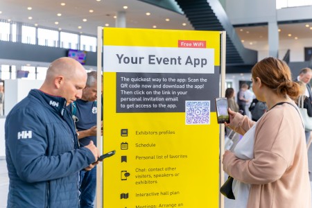 Zwei Besuchende stehen vor einem Banner und scannen einen QR-Code